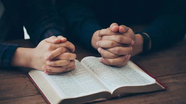 Couple with clasped hands saying their holy week prayers over the Bible