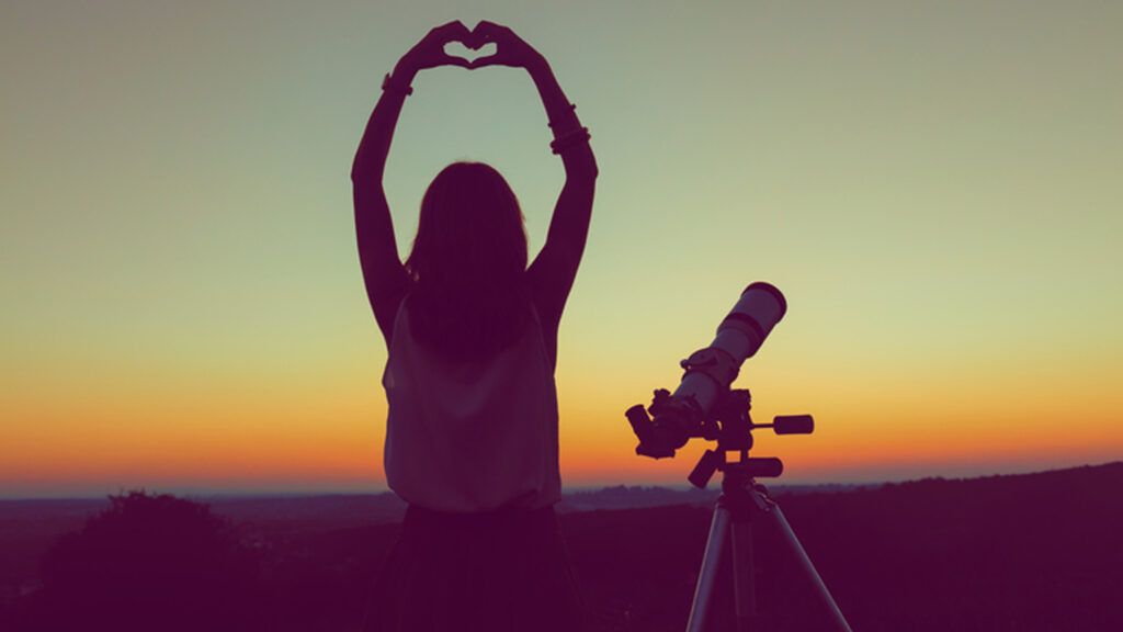 Woman with a telescope putting up a heart symbol