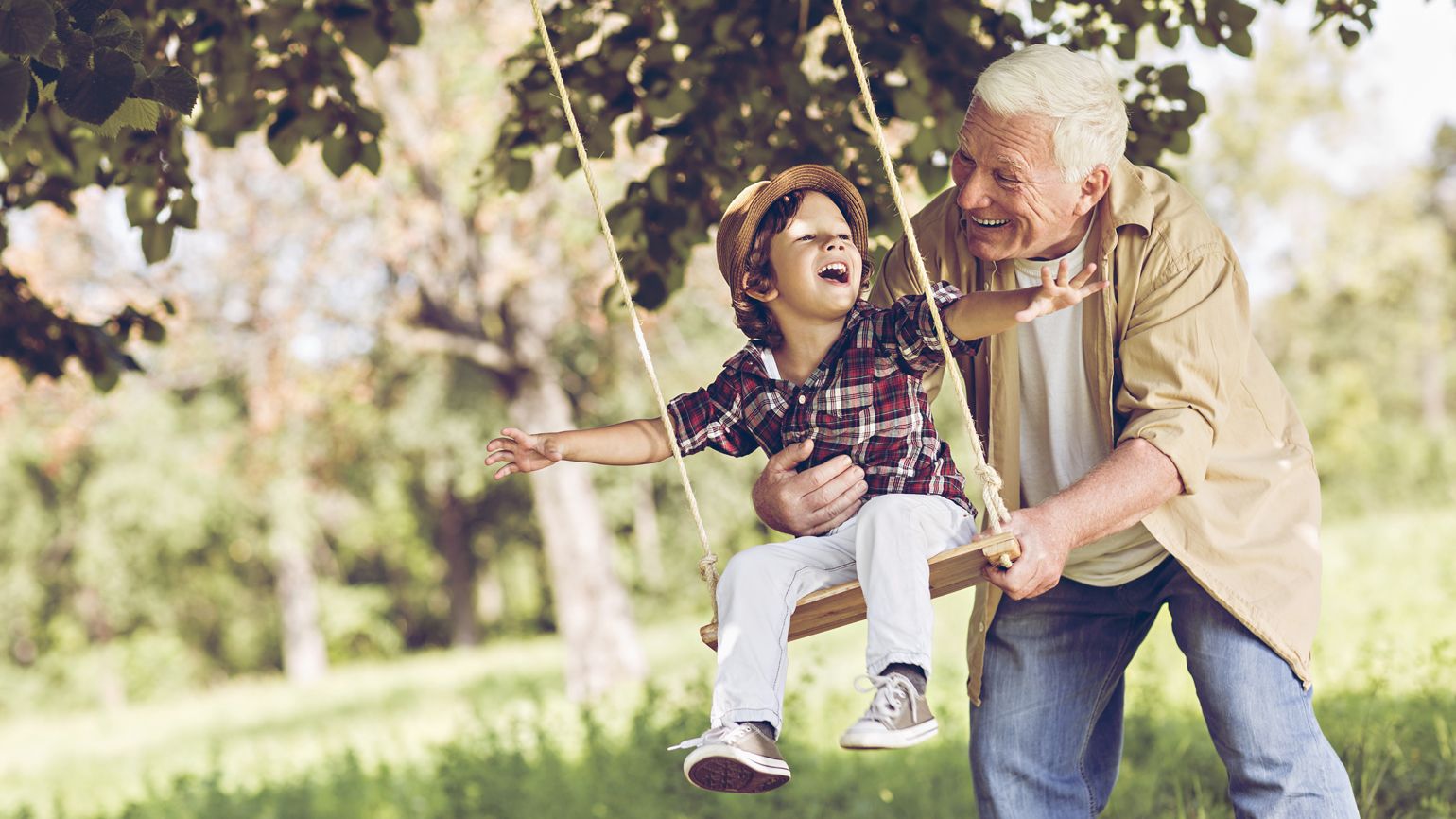 Retired grandfather pushing his grandson on a swing