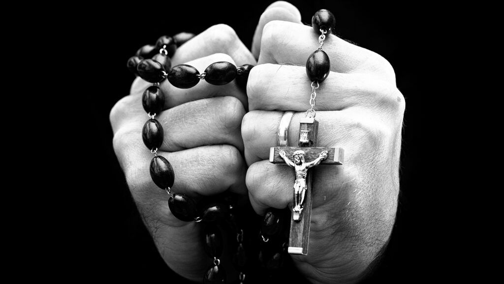 A man's hands clasp a rosary