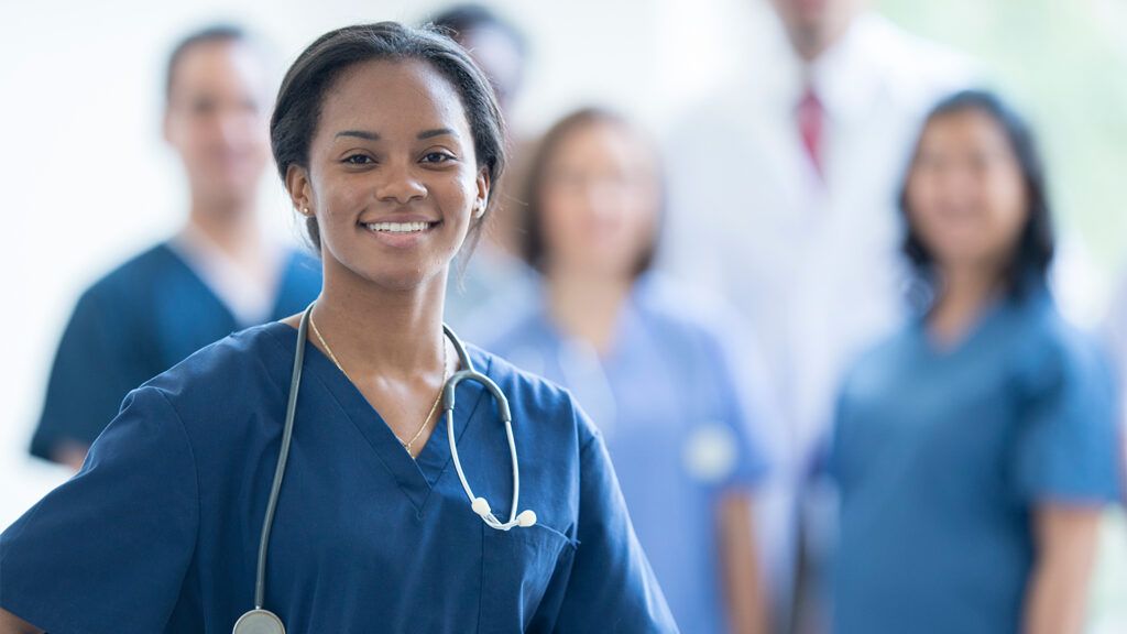 A nurse stands, smiling, as her colleagues look on