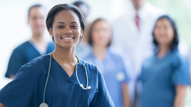 A nurse stands, smiling, as her colleagues look on