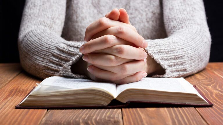 A woman's praying hands rest on an open Bible
