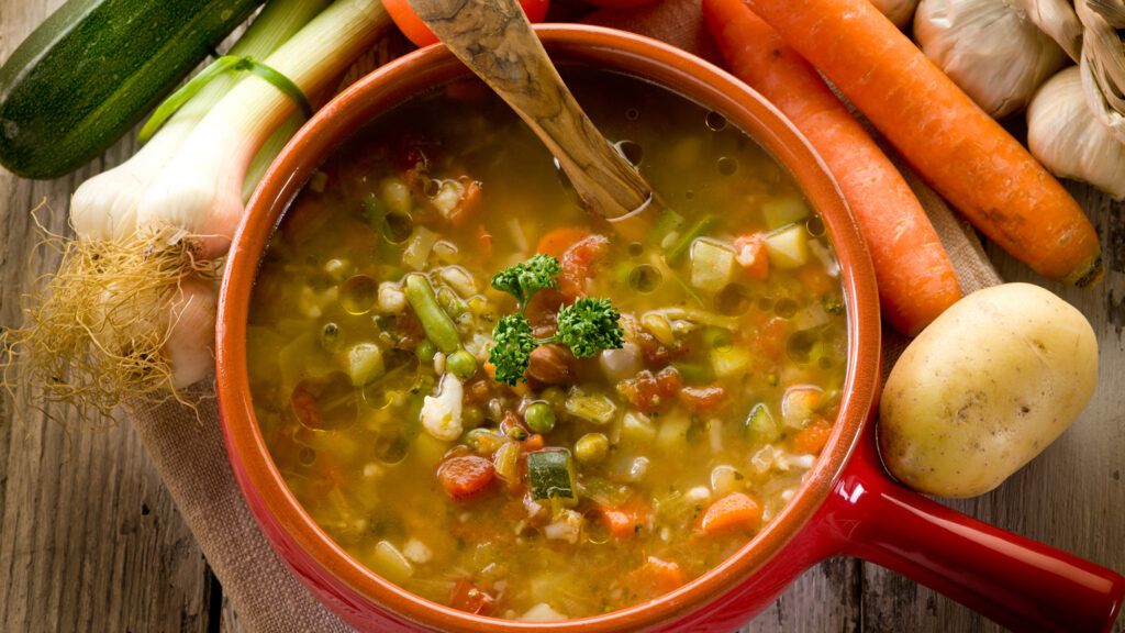 Vegetable soup in a bowl with ingredients surrounding it.