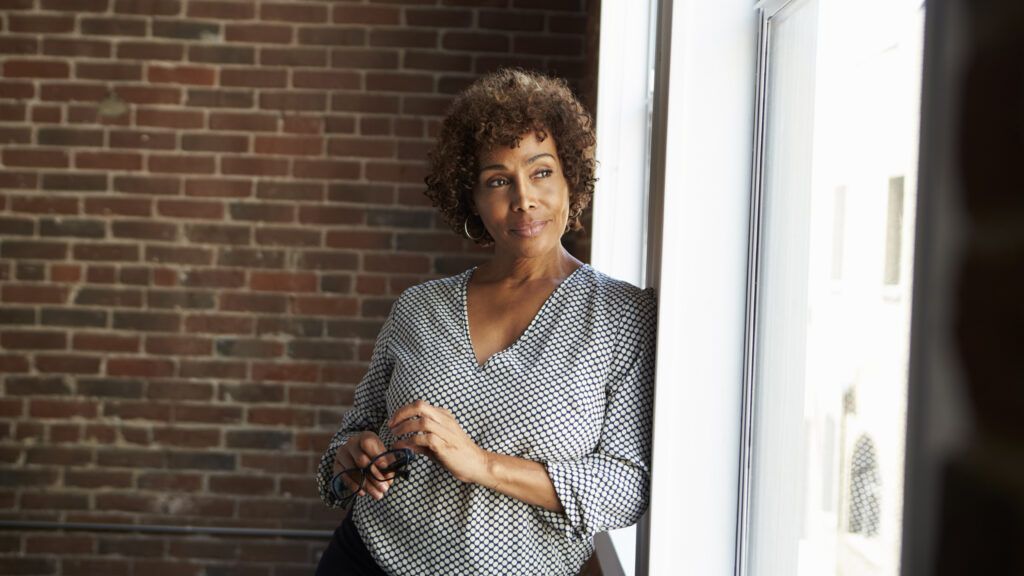 smiling woman stands by the window against a brick wall