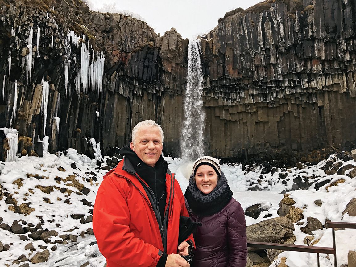 Alikay and her father pose in front of a towering waterfall
