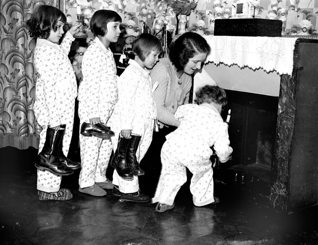 A mother helps her children place their shoes by the fireplace on Christmas Eve