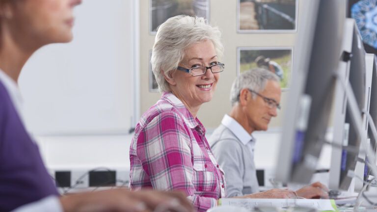 A smiling senior citizen woman learning how to use the Internet in a classroom.