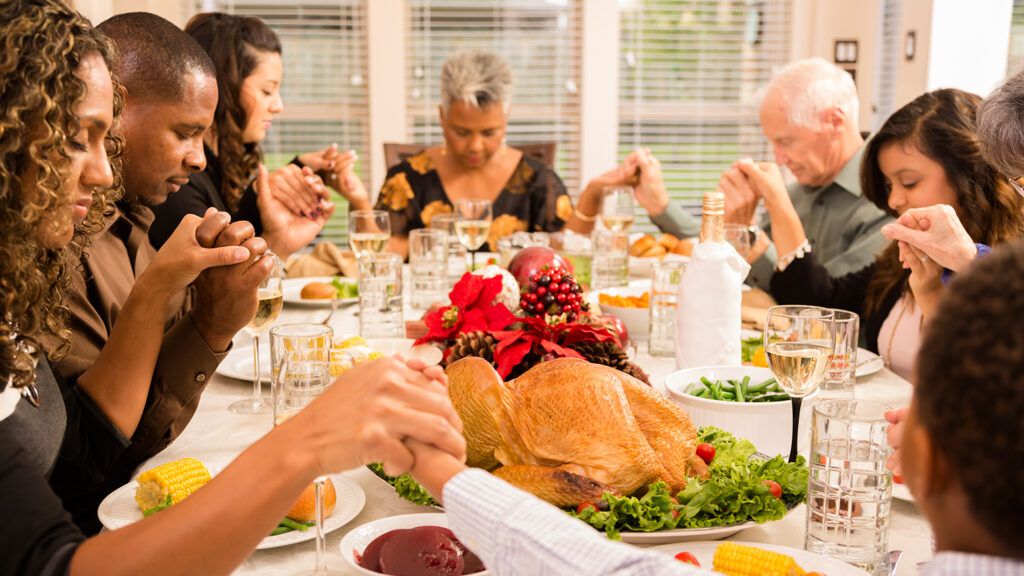 A family holds hands at the table and recites Thanksgiving meal prayers