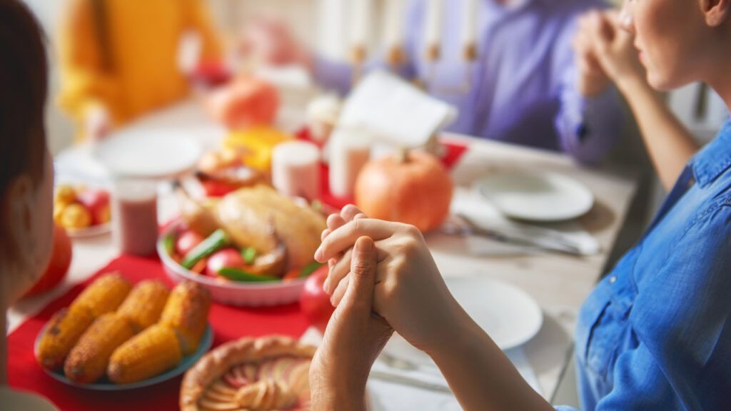A family holds hands around the table and say a Thanksgiving devotion