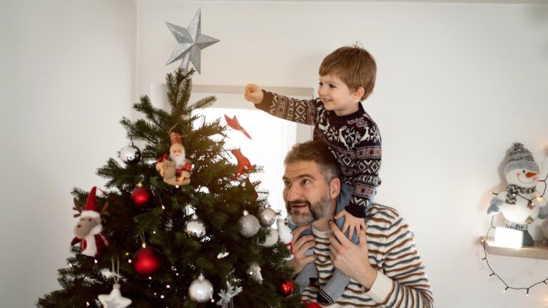 A father and son decorating a Christmas tree and looking hopeful