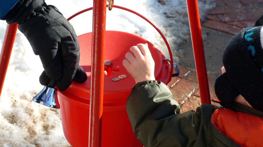 A child places money in a red charity bucket at Christmas
