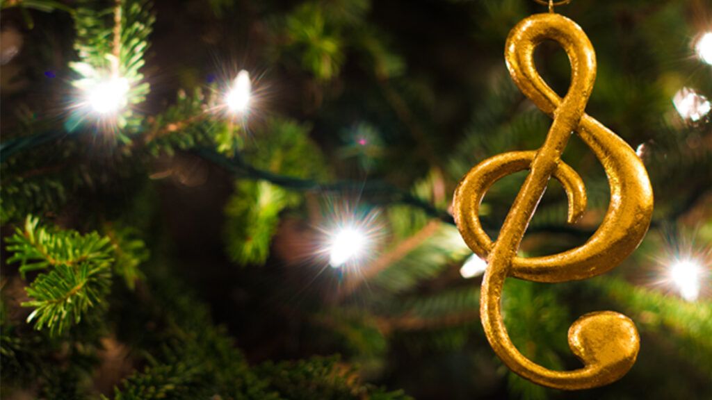 Golden music symbol ornament hanging from well-lit Christmas tree