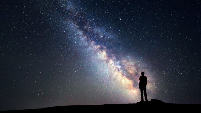 A man stands looking up at the Milky Way