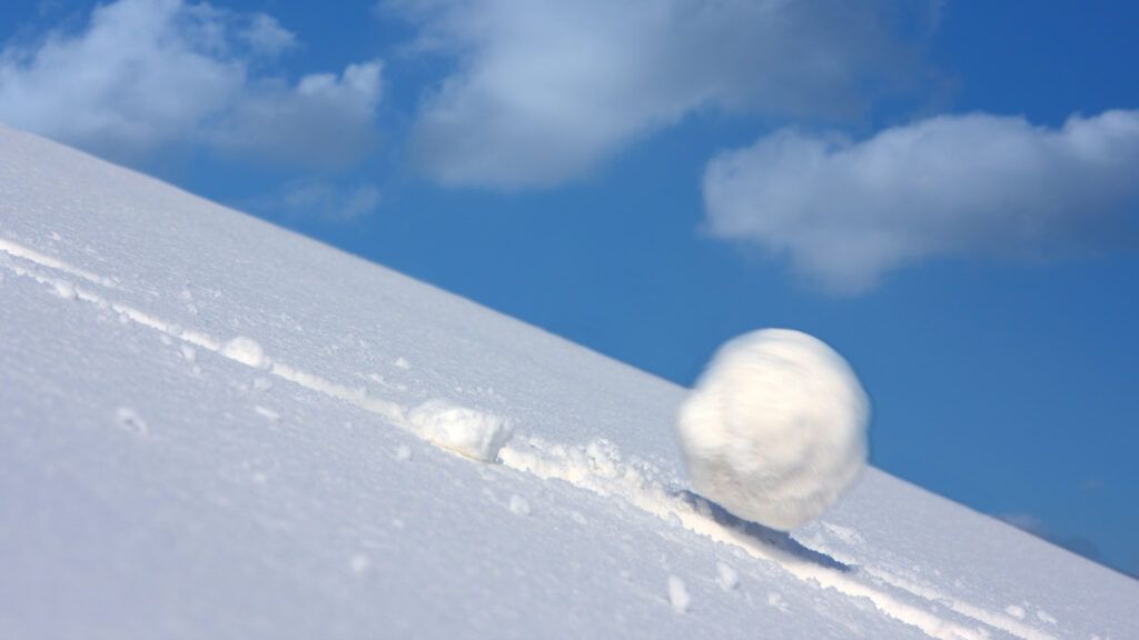 A large snowball tumbling down a snowy slope.