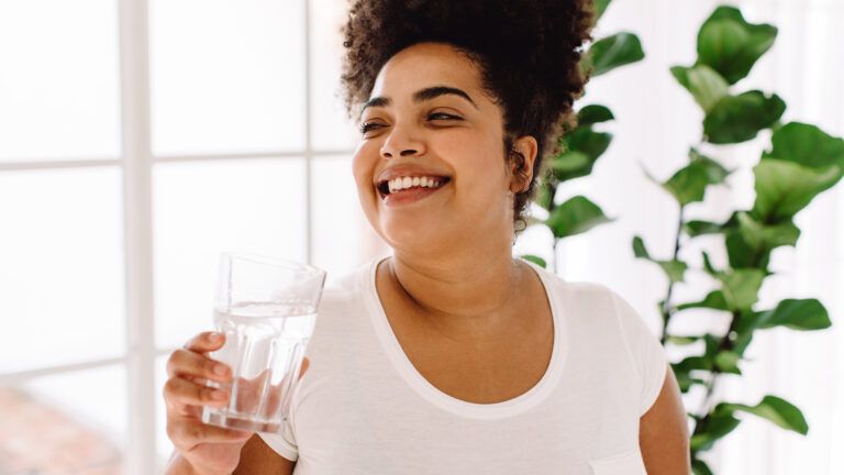 A smiling woman drinking a glass of water for her near year habit