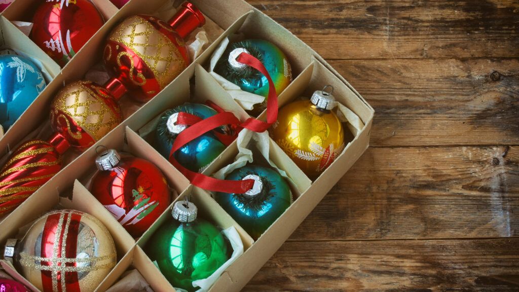 A set of vintage Christmas ornaments in a box on a wooden table.