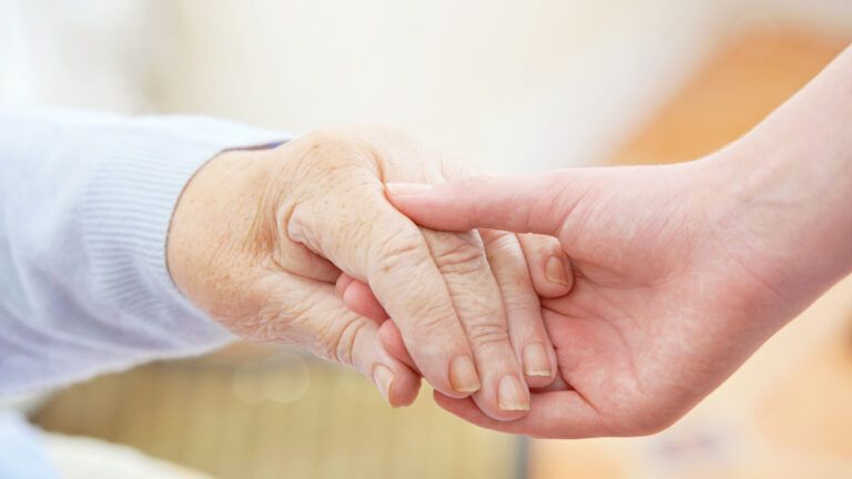 A close up of an older and younger patient holding each other's hands for help.