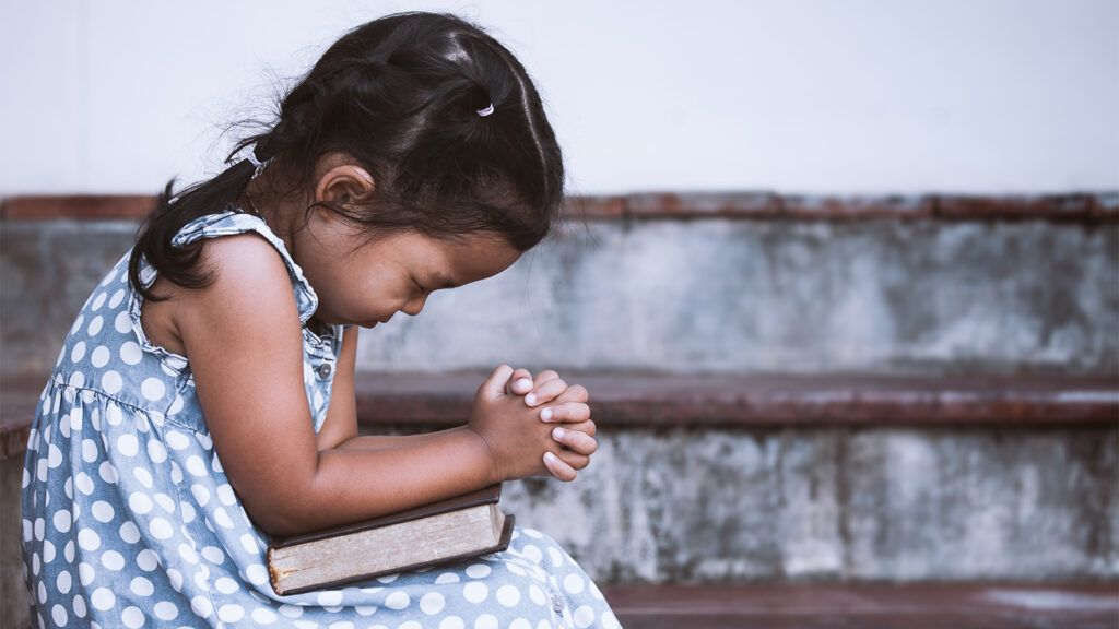 A young girl bows her head in prayer