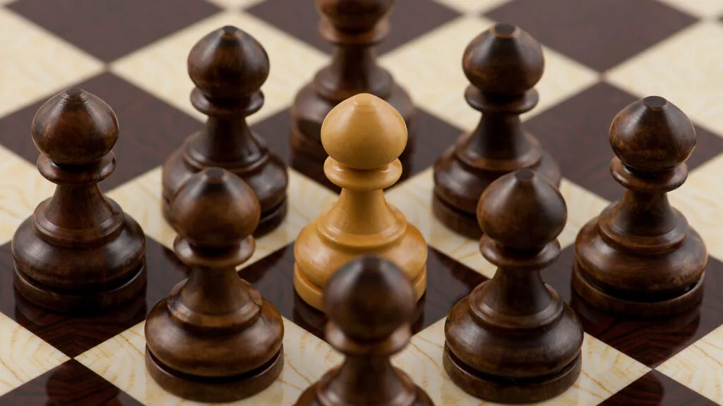 A white chess piece completely surrounded by black pieces