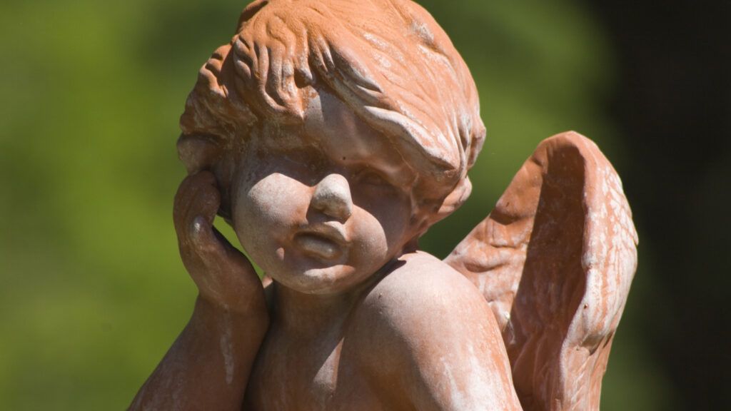 A terra cota clay angel with his hand on his chin.