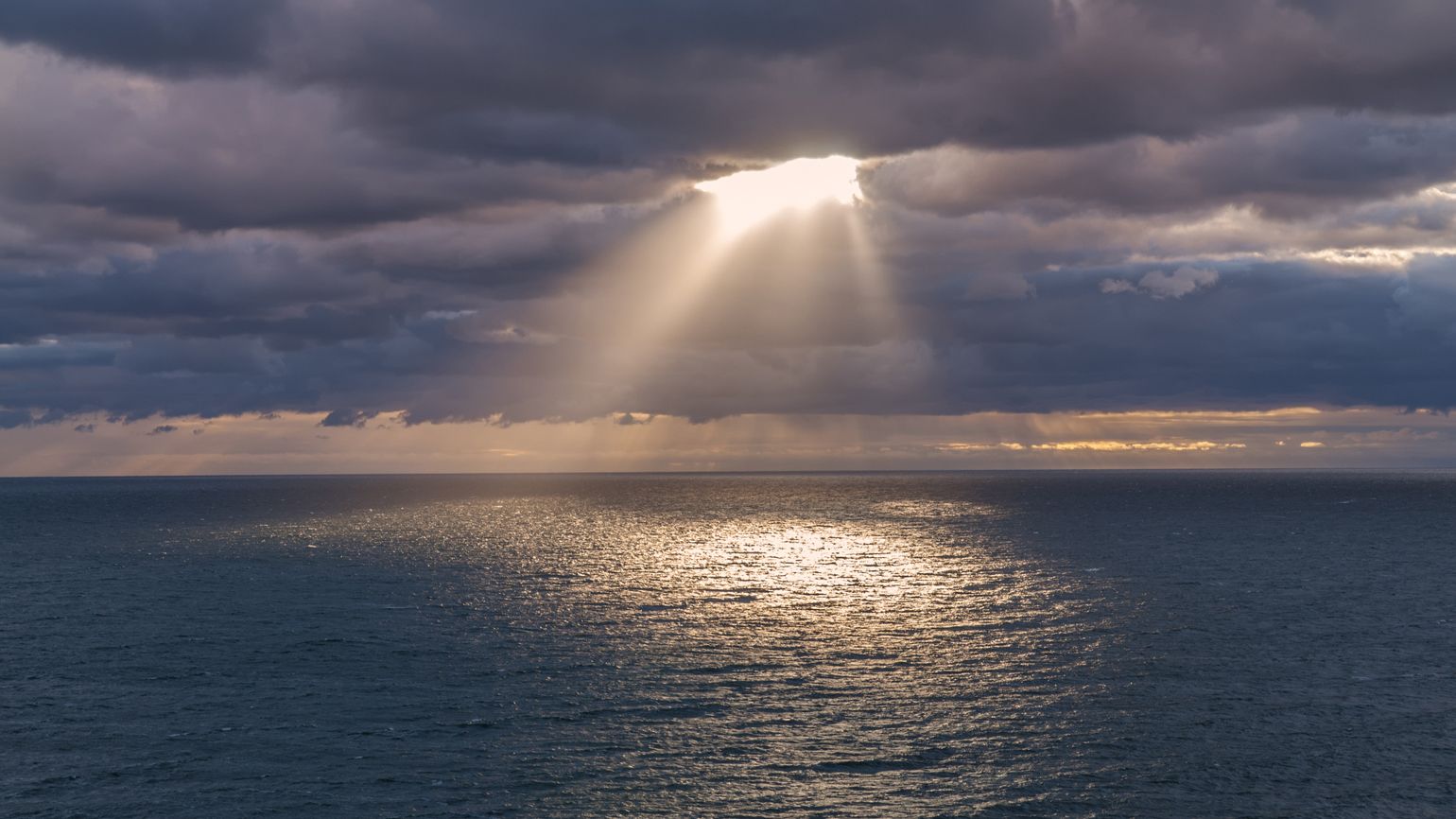 Sunrays coming through the clouds over the ocean and reflects the light in the water