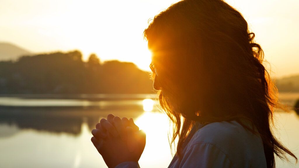 Woman praying by lake at sunrise.