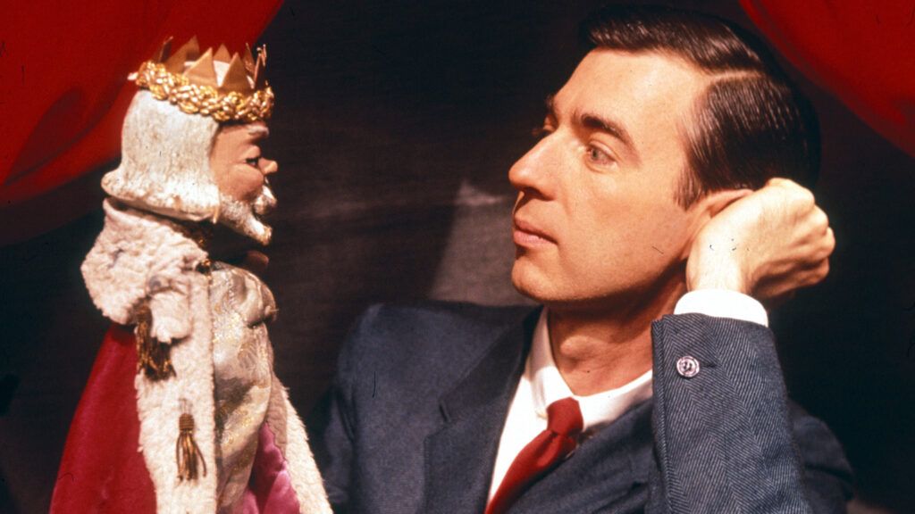 A young Fred Rogers interacts with a king puppet.