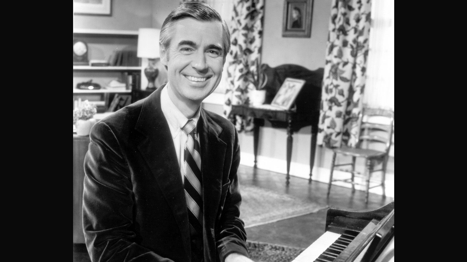A black and white photograph of young Fred Rogers playing the piano happily.