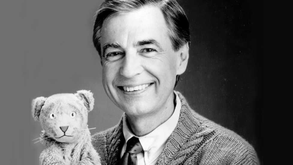 A black and white photo of Fred Rogers holding up a toy bear used in Mr Rogers' Neighborhood