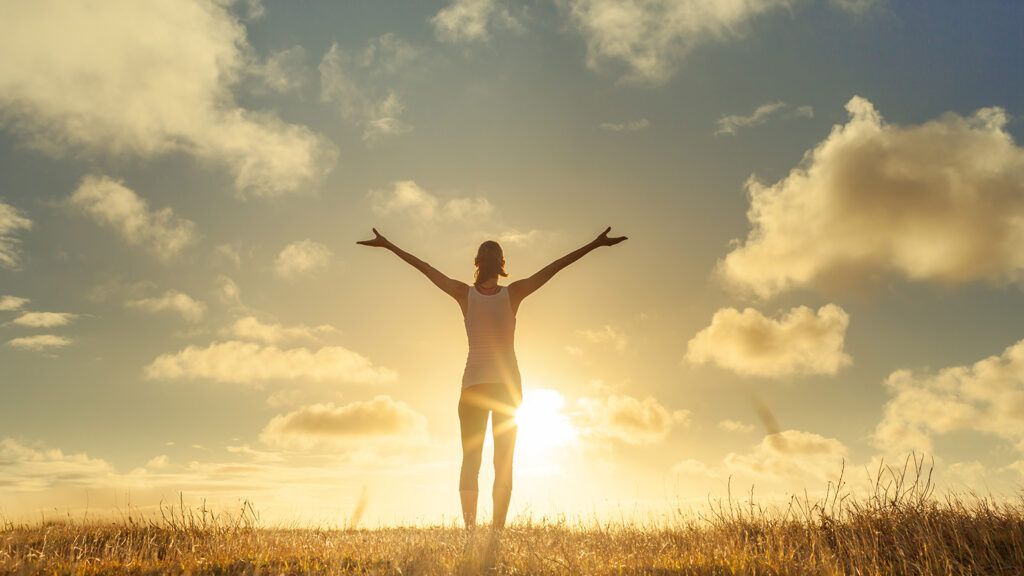 A woman stands, arms outstretched, at sunrise
