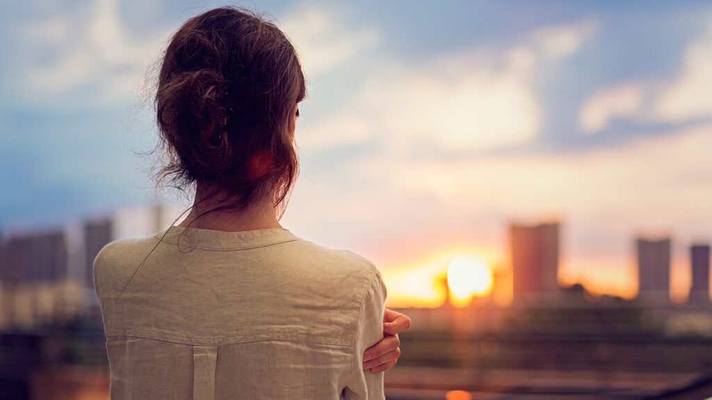 A woman gazes out over a city skyline at sunrise