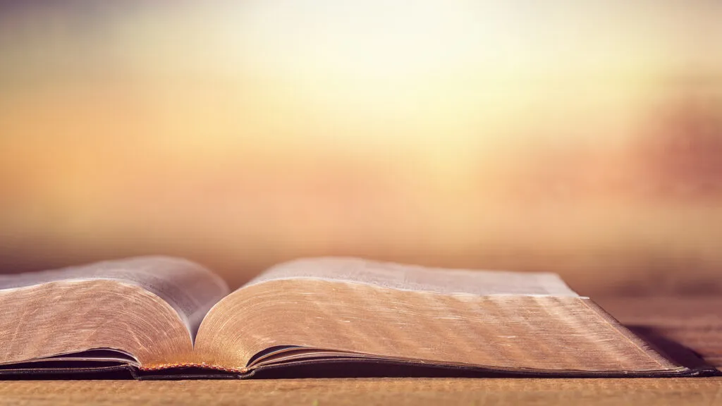 Open Bible on wooden table at sunrise