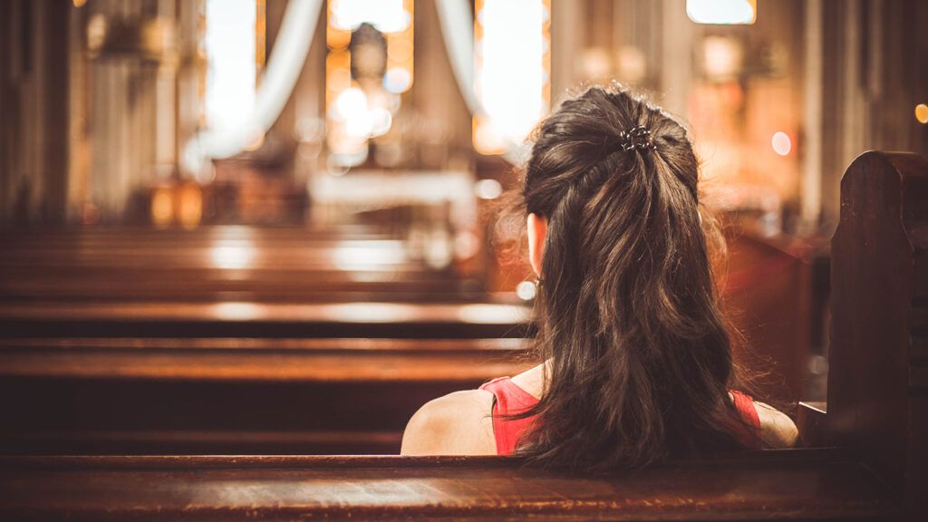 A woman sits quietly in a pew in an empty church sanctuary