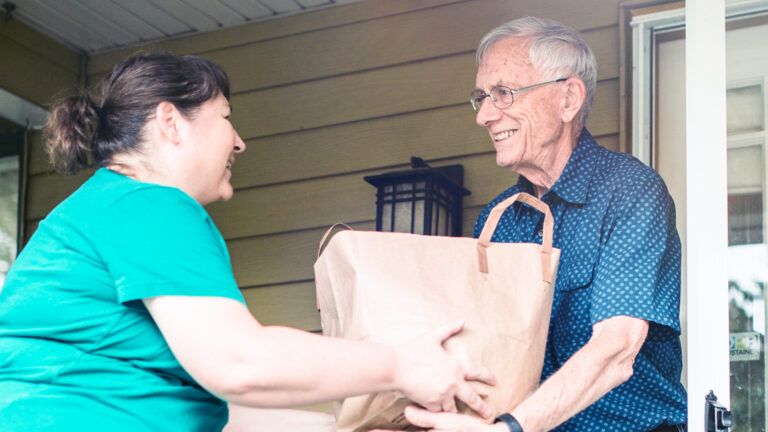 A woman brings a bag of groceries to her senior neighbor