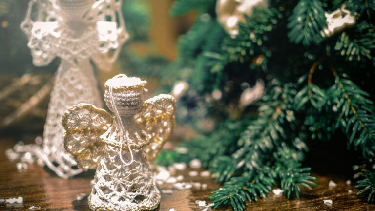 Knitted toy angels beside Christmas tree and artificial snow