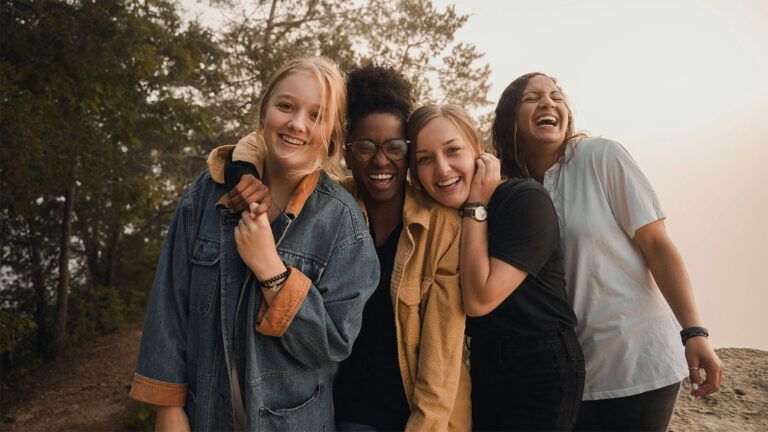 Four female friends laughing together outdoors.