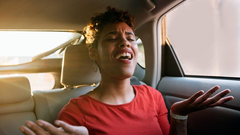 A young woman sitting in a car sings joyfully