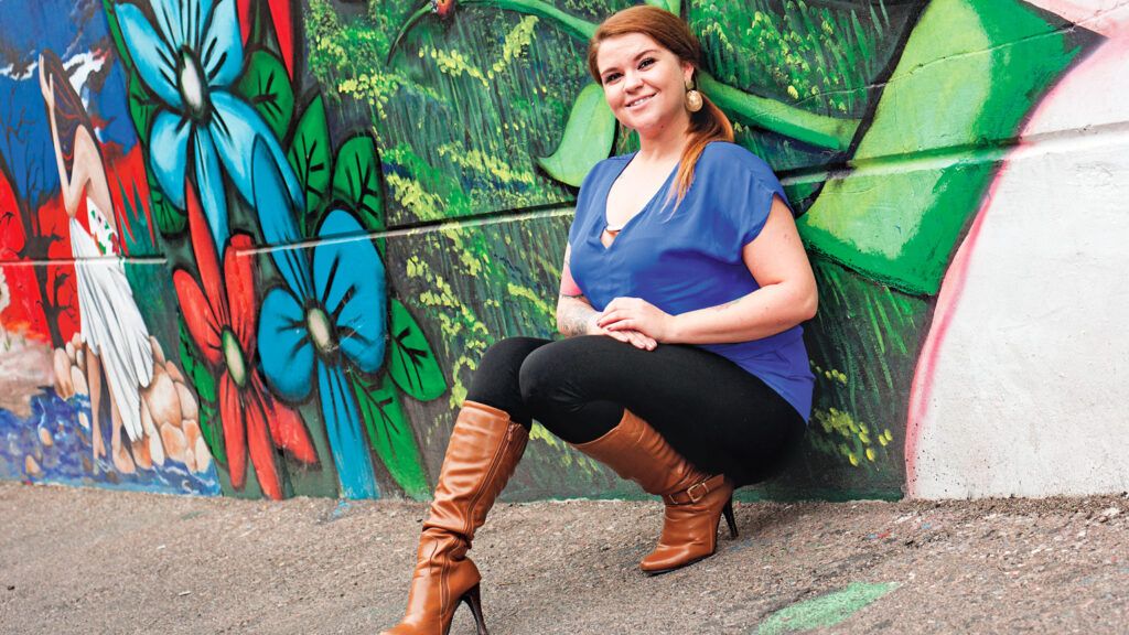 Lindsay Day-Walker sitting against a colorful mural on a brick wall.