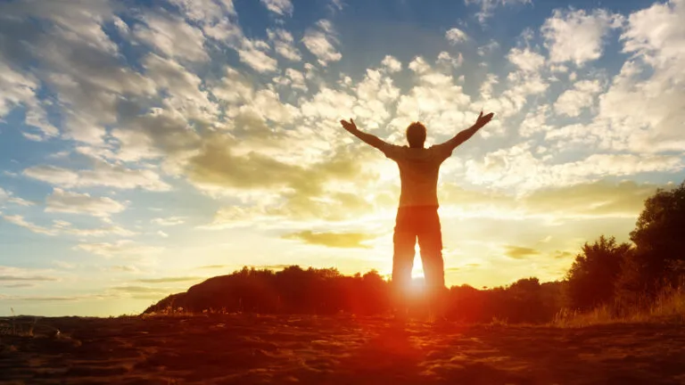 Silhouette of a man with hands raised in the sunset concept for religion, worship, prayer and praise