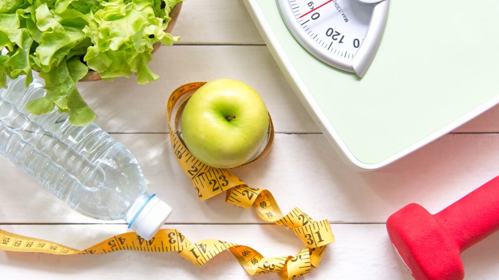 Essential tools for weight loss such as a bottle of water, a scale, and a dumbbell