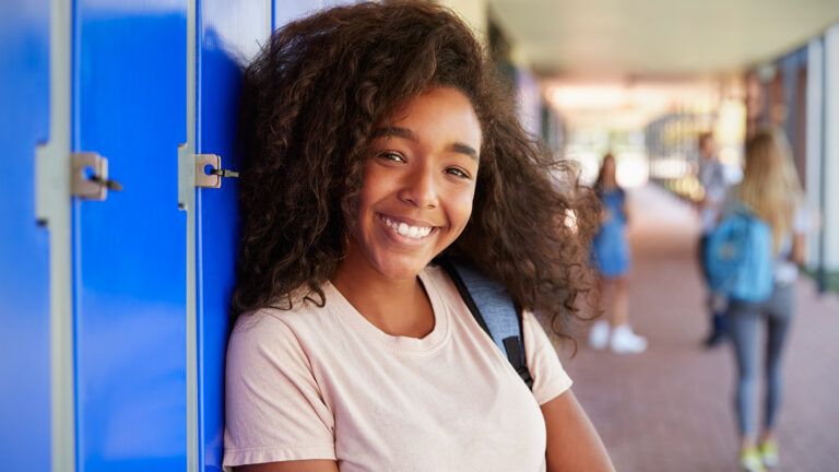 A young woman smiles by her high school locker
