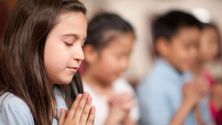 A group of children bow their heads in prayer