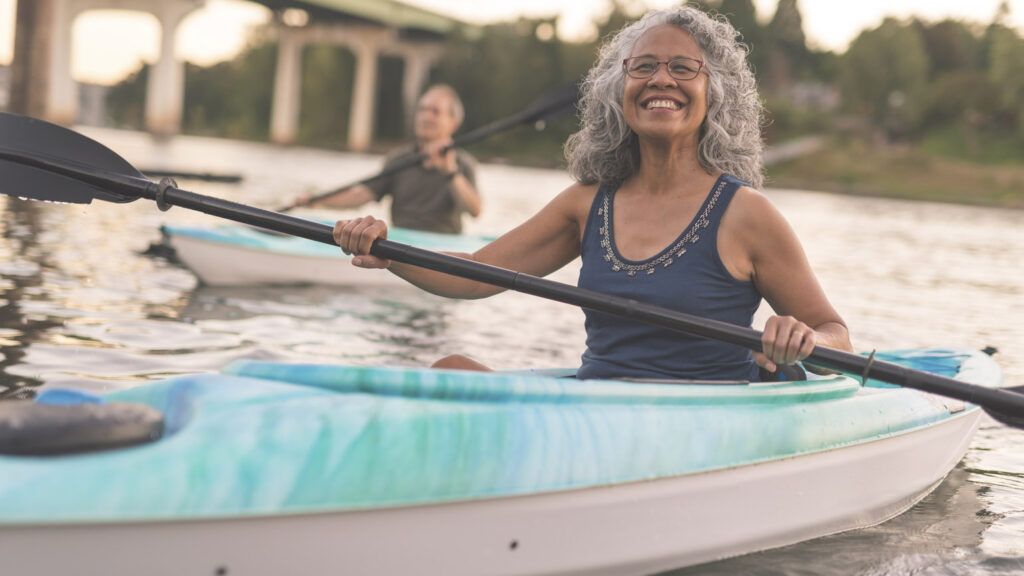 An ethnic senior woman smiles while kayaking with her husband.