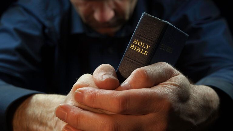 A man prays as his hands clasp a Bible