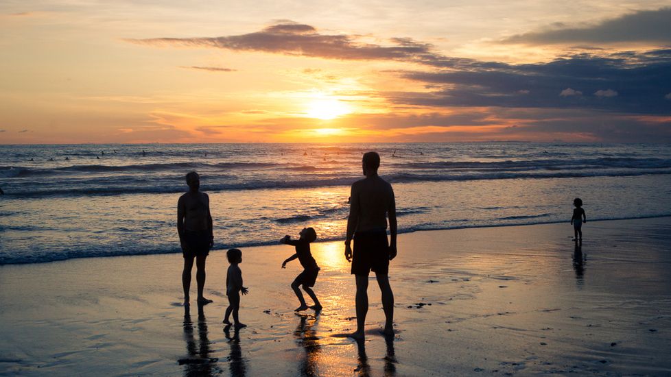 A family on the beach at sunset saying prayer for safe travel