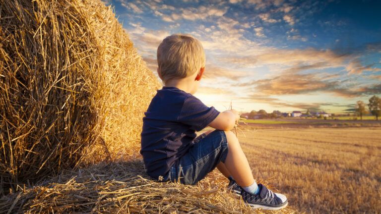 Young boy sitting on bales of straw and looking up into the sunset
