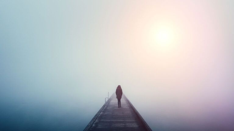 A woman stands looking out from a foggy pier
