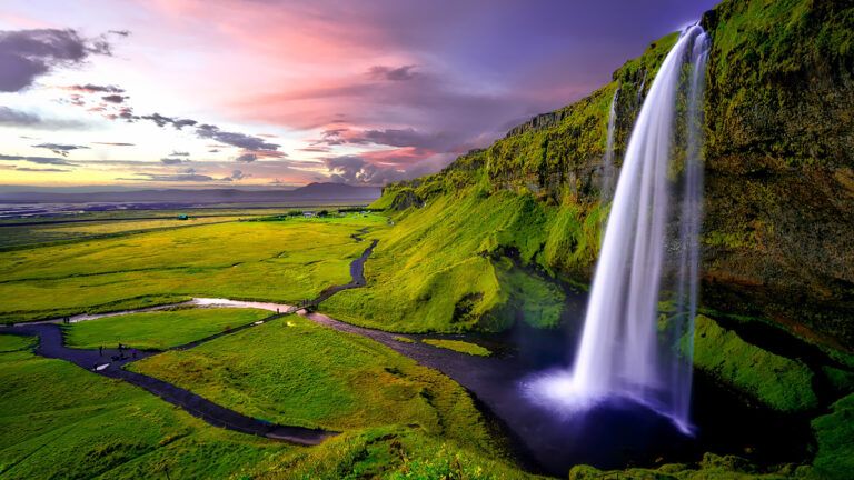 A scenic waterfall with the sun setting in the distance