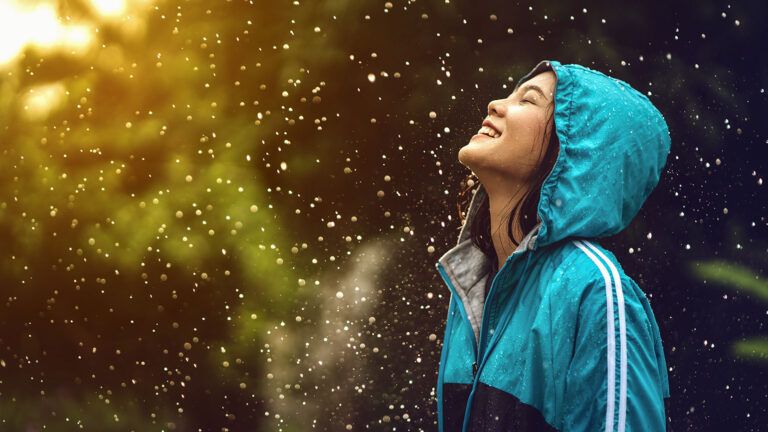 A joyful woman raises her face to the sky in the rain